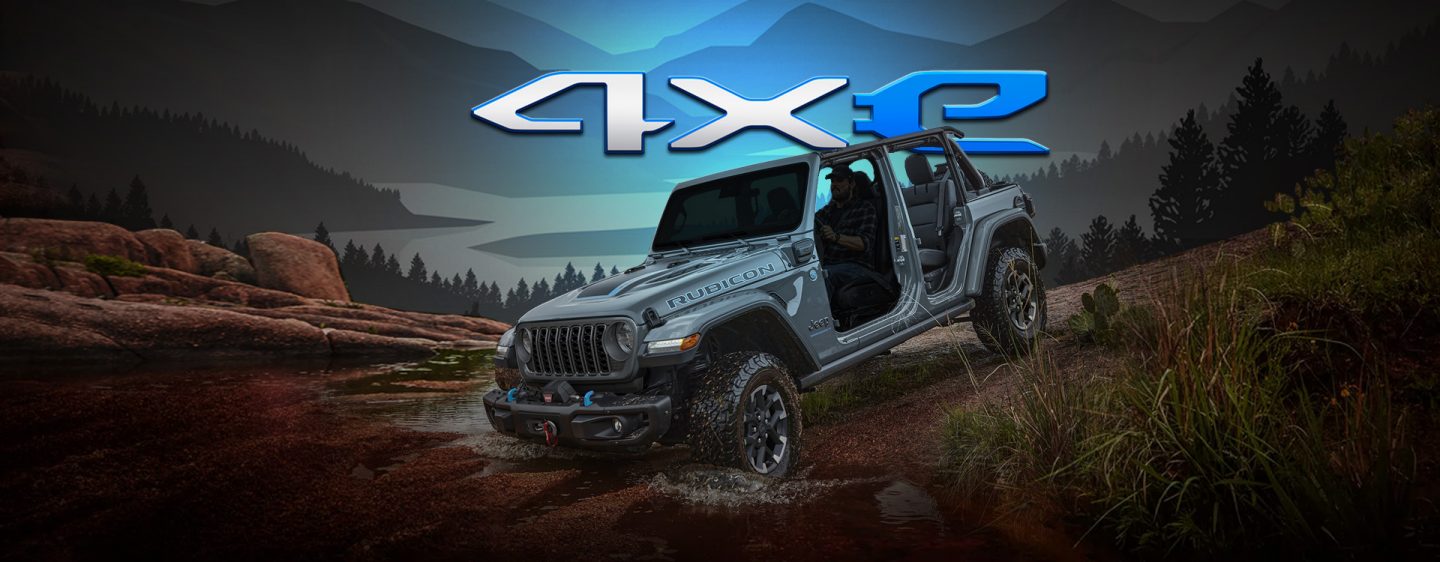 A silver 2024 Jeep Wrangler Rubicon 4xe with its doors removed, descending a hill as it enters a stream. Mountains are drawn in the background. 4xe.