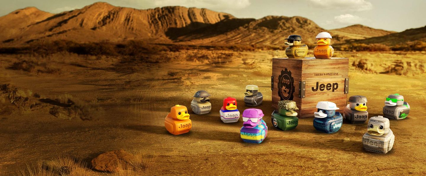 12 distinctly different Jeep ducks in the desert, scattered around a small wooden crate stamped with Jeep logos and symbols.